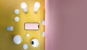 Slimme lampen, slimme stekkers en een smartphone op een gele en roze achtergrond